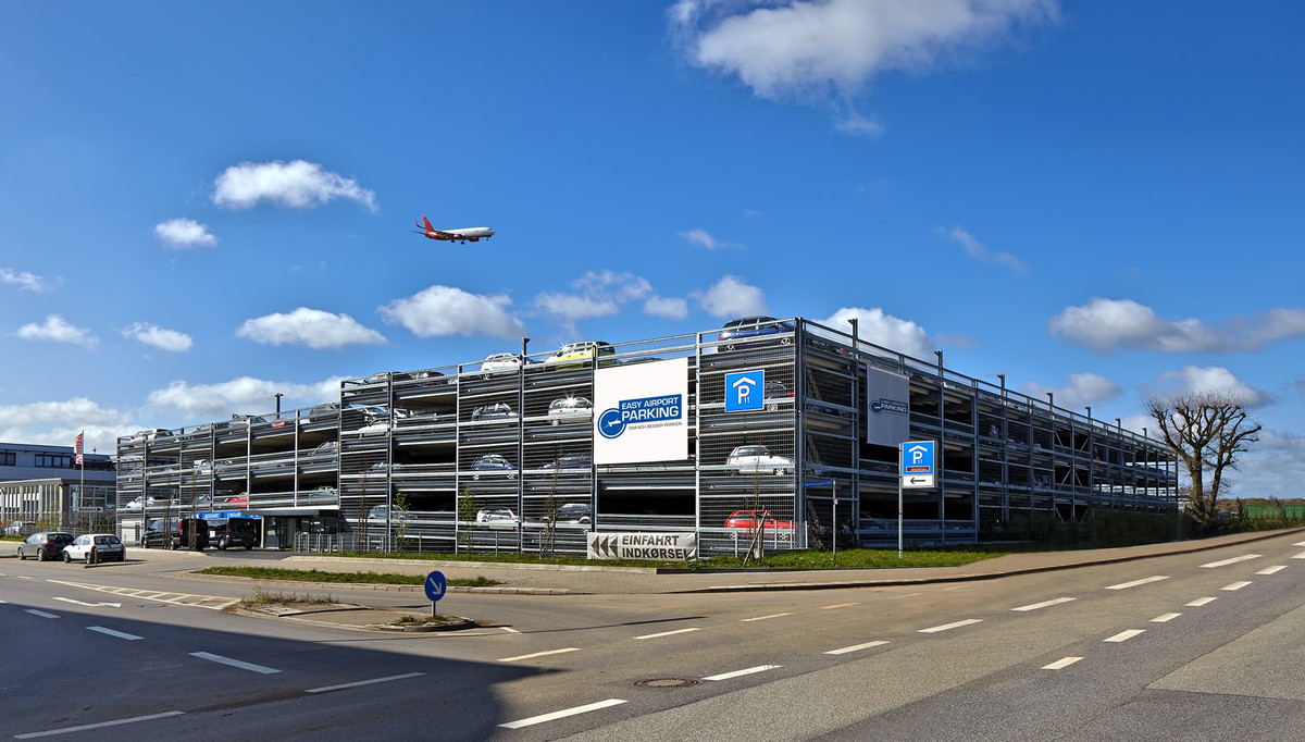Straataanzicht van de meerlaagse Easy Airport Parking parkeergarage met landend vliegtuig bij luchthaven Hamburg (HAM)