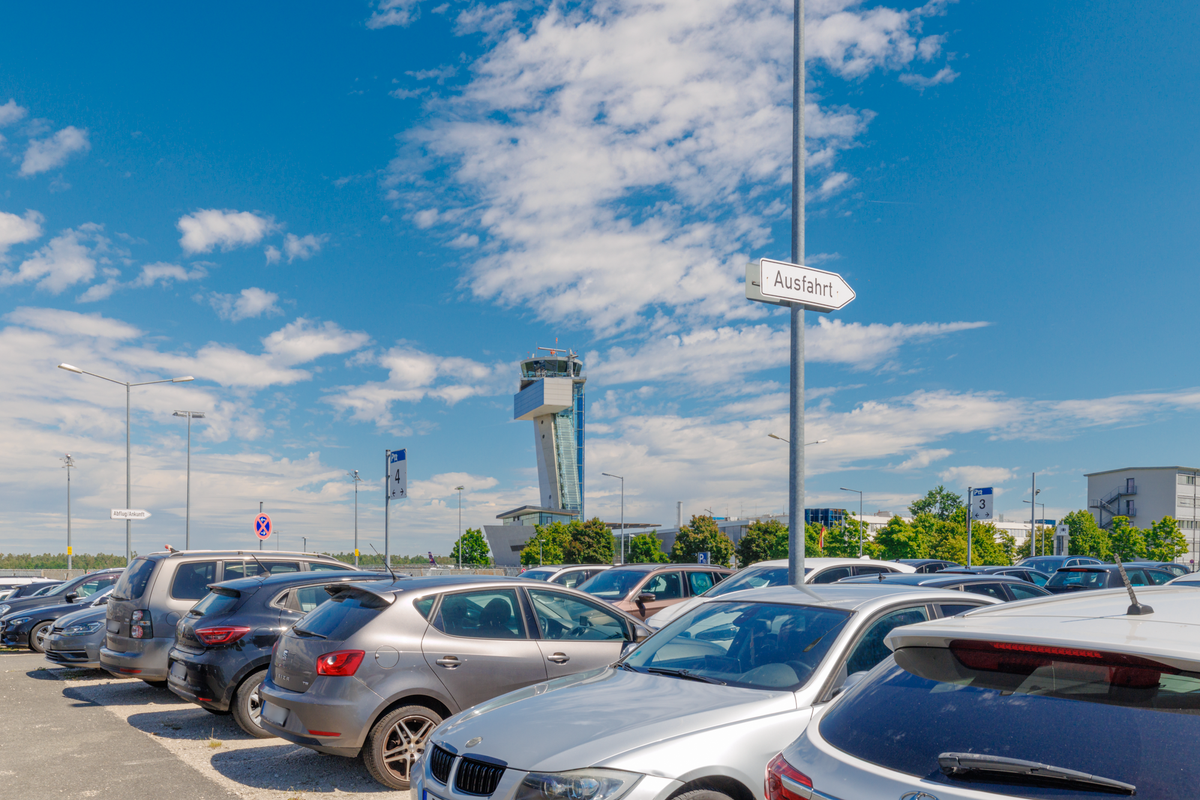 Parkende Autos auf dem Easy Airport Parking Parkplatz am Flughafen Nürnberg (NUE) mit Flughafen Tower im Hintergrund.